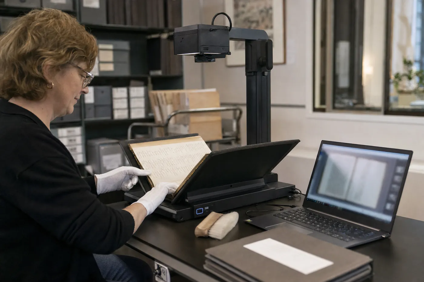 An archivist in white cotton gloves scanning an old ledger with an overhead book scanner