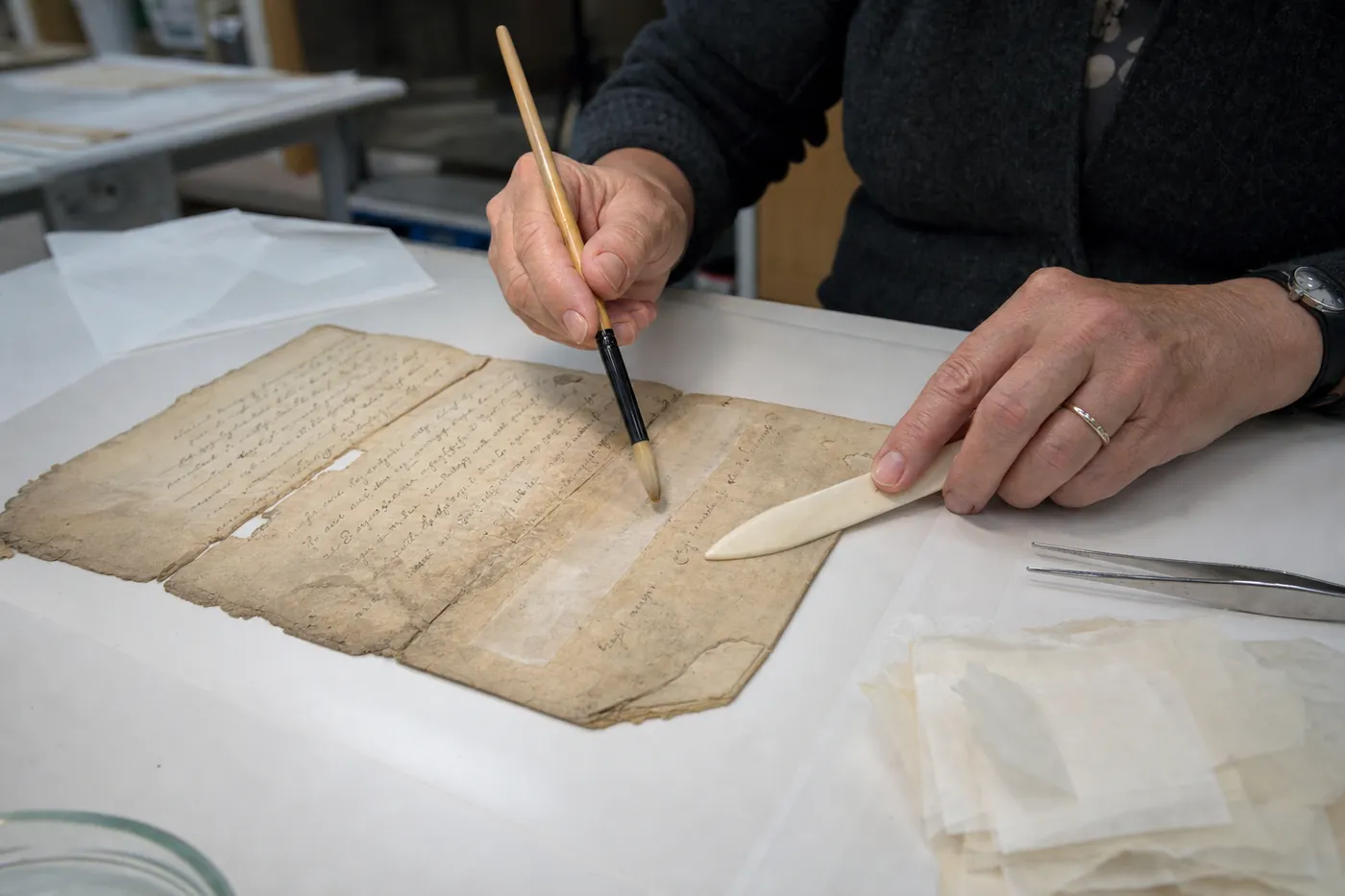 A conservator repairing a torn old handwritten document with thin Japanese paper